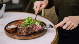 female hands in a restaurant at the table cut beef striploin steak