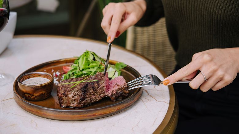 female hands in a restaurant at the table cut beef striploin steak