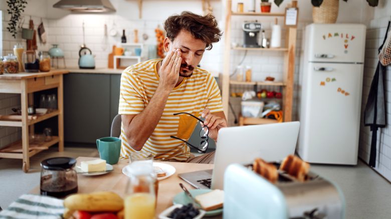 Exhausted young man working from domestic kitchen