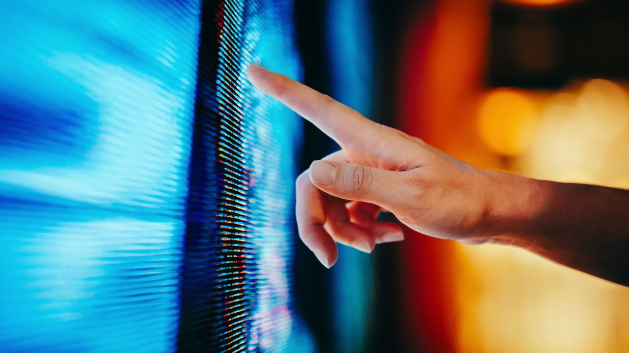Close up of woman's hand touching illuminated and multi-coloured LED display screen, connecting to the future. People, lifestyle and technology