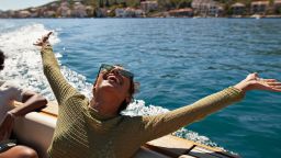 Happy young woman with arms raised in motorboat enjoying sunny day