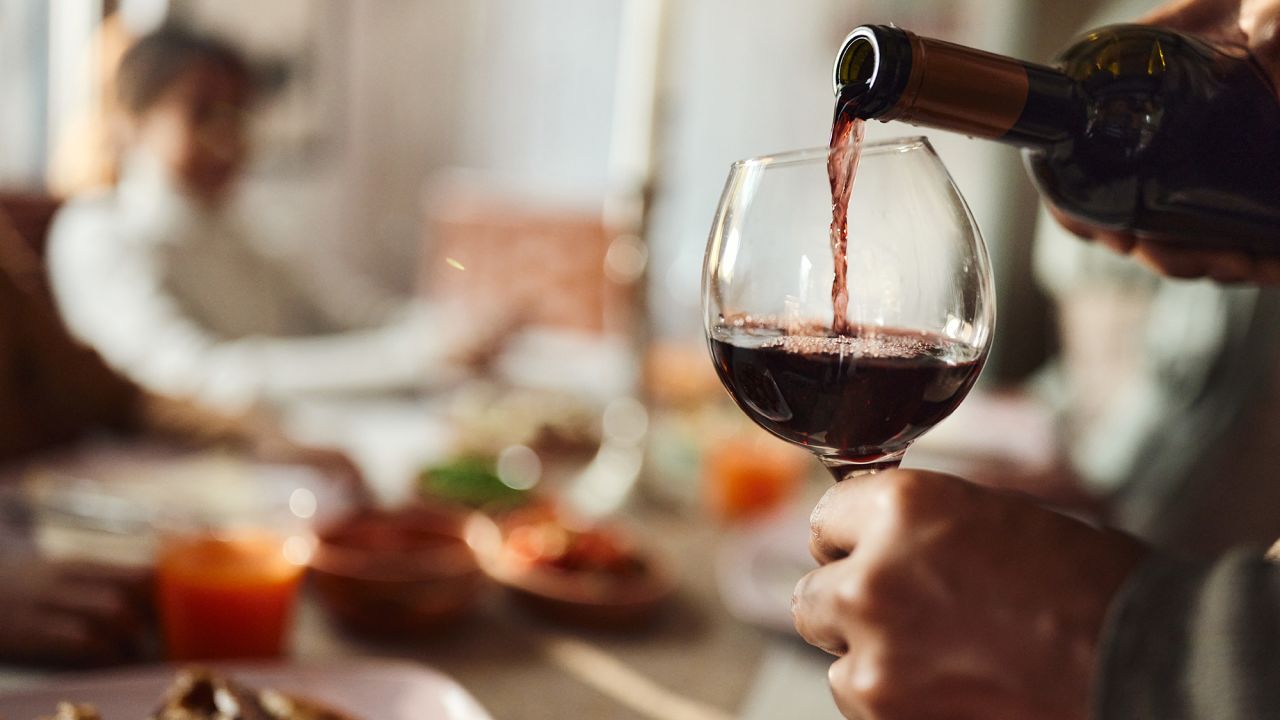 Close up of unrecognizable black man pouring red wine into a glass in dining room.