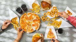 Flat-lay of friends group eating burgers, fries, onion rings, pizza, drinking cola at outdoor party over table background, top view. Fast food dinner from delivery service.Fast food and unhealthy eating concept