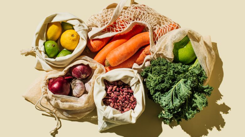 Variety Fresh of organic fruits and vegetables and healthy vegan meal ingredients in reusable eco cotton bags on beige background . Zero waste shopping concept. Healthy food, clean eating, eco friendly, no plastic. Flat lay, top view