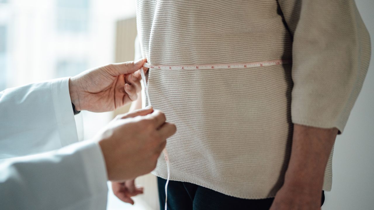 Midsection of doctor measuring patient’s waist with tape measure. Healthcare consultation. Health and wellbeing.