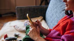 A side view of an unrecognizable Caucasian mother using her smartphone while relaxing at home with her little child.