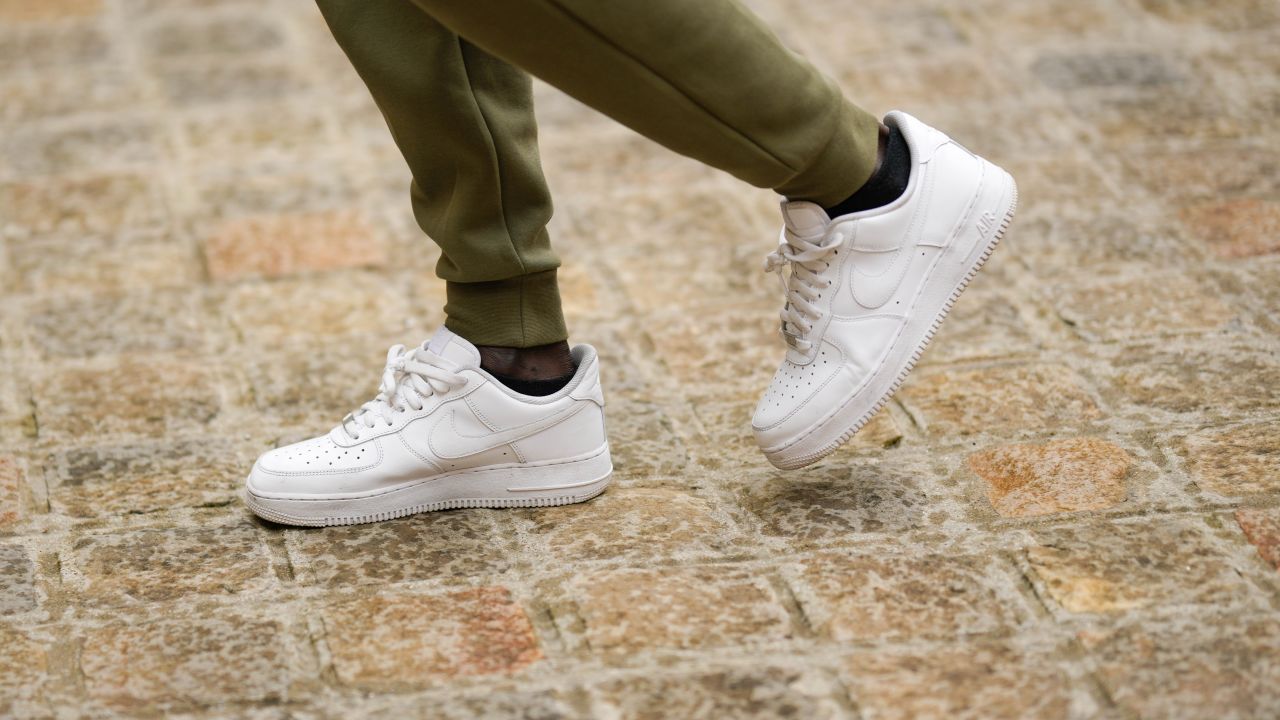 A guest wears green and khaki bicolored pattern sport pants from Nike, white shiny leather laces Air Force One sneakers from Nike, outside the COS show, on April 26, 2023 in Paris, France.