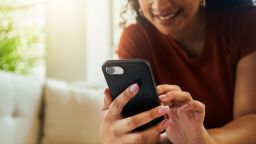 A young woman sitting on her sofa while smiling and texting on her mobile phone. Stock photo