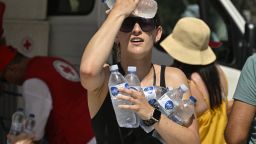 A woman cools off with cold bottles of water, distributed by the hellenic red cross organization near the entrance of the Acropolis archeological site in Athens on July 20, 2023, as the country is hit by a new major heatwave. Archaeological sites, including the Acropolis, will be closed during the hottest hours of the day due to the new heatwave, Greece announced on July 20. (Photo by Louisa GOULIAMAKI / AFP) (Photo by LOUISA GOULIAMAKI/AFP via Getty Images)