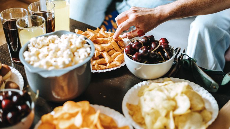 Happy pizza time: Picture of hands of unrecognizable friends hanging out together in living room having yummy snacks, pizza, and drinks in front of them on table and enjoying being together in Gen Z gang
