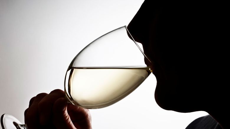 Sihouetted profile of someone drinking a glass of white wine.