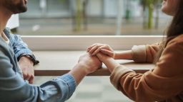 Close-up of a smiling young couple holding hands together while sitting by a window in a cafe during a date