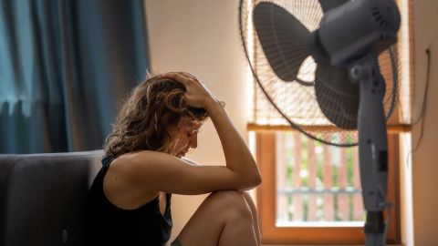 Young woman suffering from heat sitting at home on the floor in front of a fan