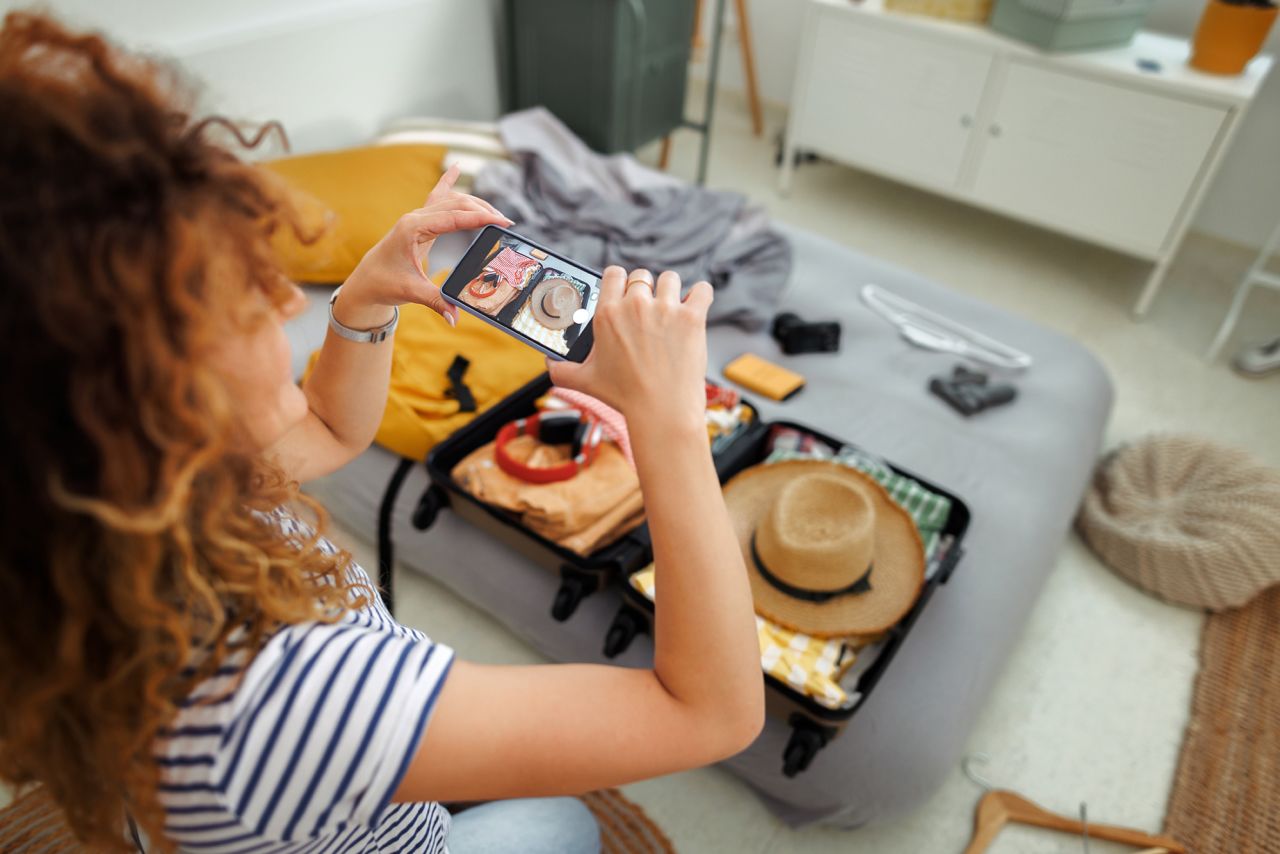 A woman takes photos of her packed suitcase at home.