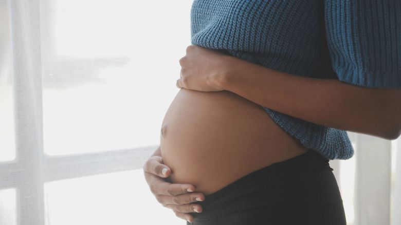 Happy pregnant woman touching belly in front of white wall