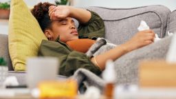 Sick, pills and black woman on sofa with tissue paper, flu and headache from viral infection in her home. Bacteria, migraine and African lady with virus, fatigue and nausea medicine in living room