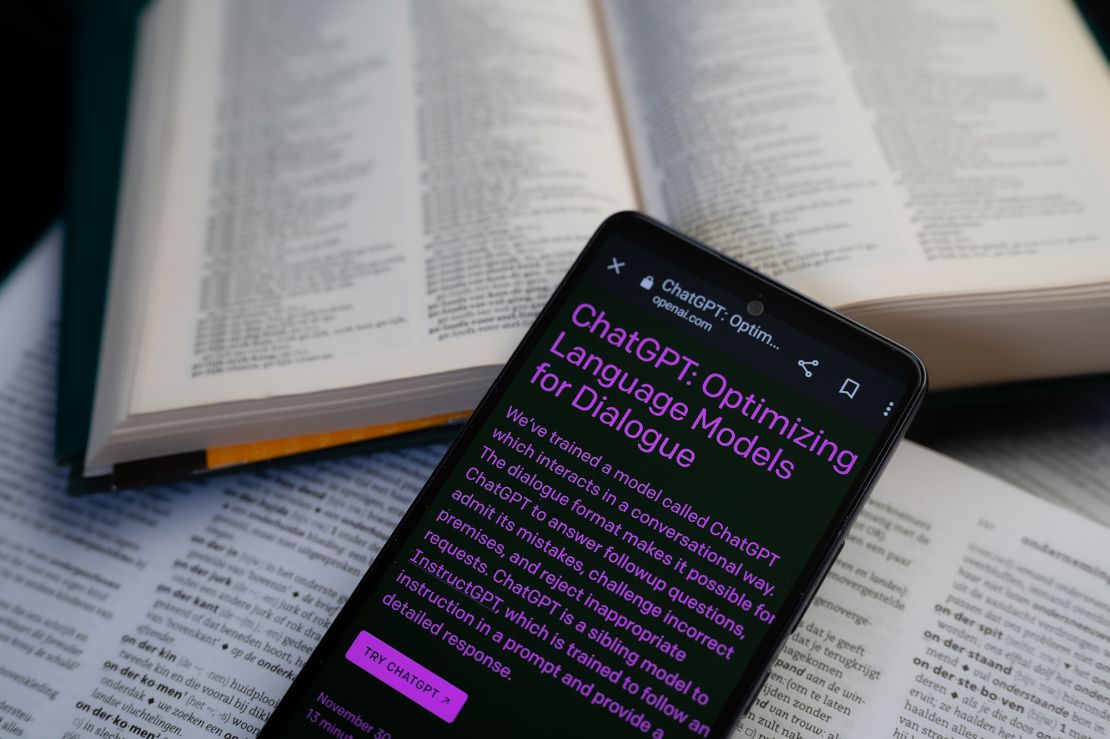 Open Ai page displayed on a smart phone with a dictionary book, seen in this photo illustration.