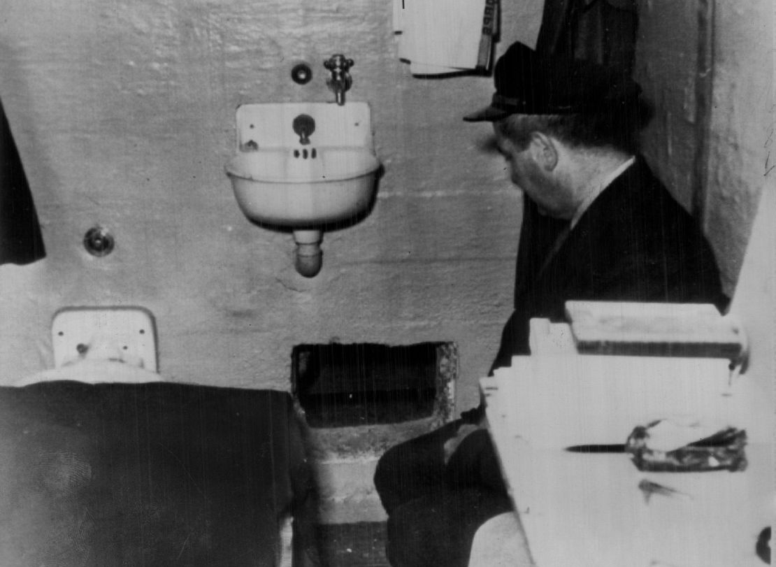 A prison attendant kneels at a hole in Frank Morris' prison cell through which he, John and Clarence Anglin had escaped. Prison officers reported that the hole was dug with broken spoons.