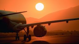 The close-up photo captures a captivating moment as the airplane's engine emanates intense heat on the runway, set against the backdrop of the immense setting sun. The engine's vibrant energy contrasts with the serene beauty of the sunset, evoking the anticipation of an imminent takeoff.