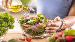 The final preparation of a healthy salad and at the end the woman pours olive oil.