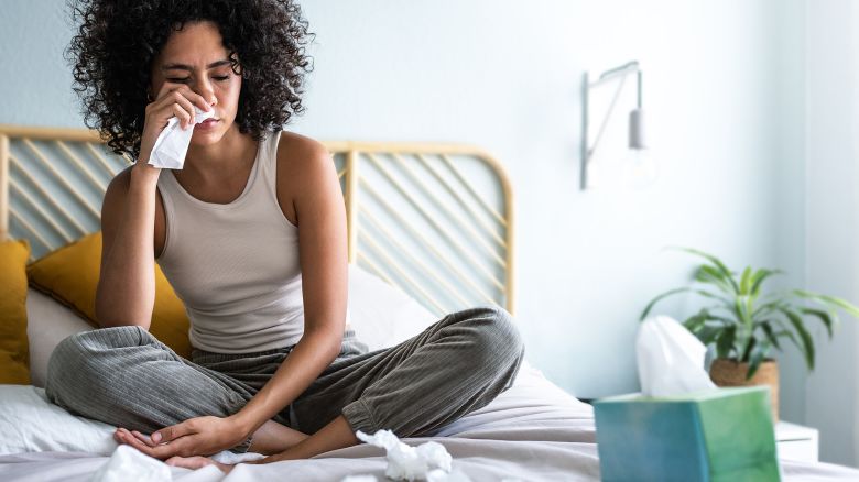 Young multiracial latina woman suffering from a cold, blowing nose with paper tissue. Cold and sickness concept.