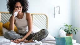 Young multiracial latina woman suffering from a cold, blowing nose with paper tissue. Cold and sickness concept.