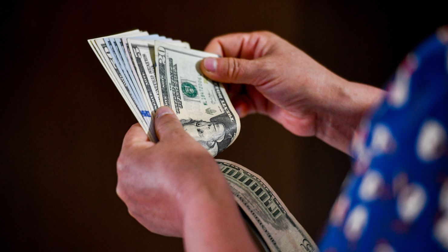 In this photo illustration, a person holds 5 and 20 US dollar bills in their hands.