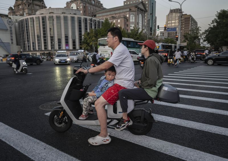 A boy looks towards a shopping small LCD screen as he waits while riding with his parents on a scooter