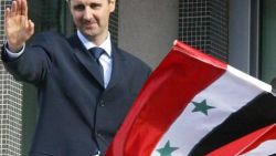 El presidente sirio Bashar al-Assad saluda a la multitud mientras unos niños ondean su bandera nacional durante una manifestación en Damasco 09 de marzo de 2005. Decenas de miles de personas convergieron hoy en Damasco en una muestra de apoyo a Bashar al-Assad, sometido a una intensa presión internacional por el dominio de su régimen sobre el vecino Líbano