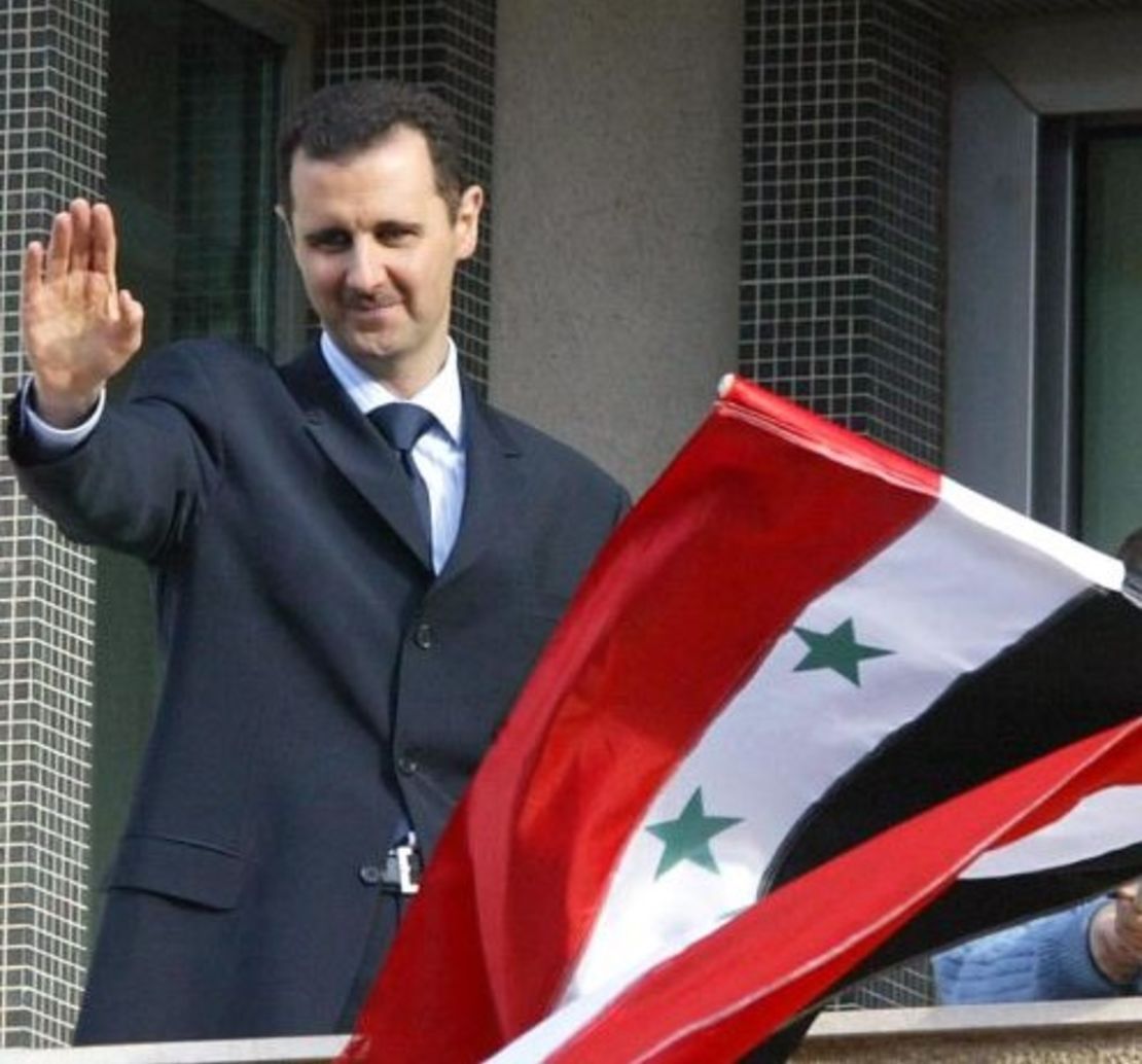 El presidente sirio Bashar al-Assad saluda a la multitud junto a la bandera de Siria durante una manifestación en Damasco 09 de marzo de 2005.