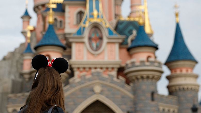 Visitors wearing emblematic Mickey and Minnie Mouse ears look on, in front of the Sleeping Beauty-inspired castle in Disneyland Park at Disneyland Paris, in Marne-la-Vallee, east of Paris, on October 16, 2023. The Walt Disney Company celebrates its 100th anniversary on October 16, marking the occasion with the release of a short film featuring more than 500 characters from 85 films. Disneyland Paris marked that anniversary with a parade showcasing a hundred of Disney's characters.