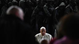 El papa Francisco se sienta frente a una escultura de bronce llamada "Ángeles sin darse cuenta" que representa a migrantes en un bote del artista canadiense Timothy Paul Schmalz durante una oración dedicada a los migrantes y refugiados en la plaza de San Pedro en el Vaticano el 19 de octubre de 2023.
