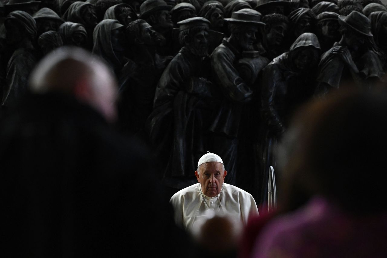 El Papa Francisco se sienta frente a una escultura de bronce llamada 'Ángeles sin darse cuenta' que representa a migrantes en un bote del artista canadiense Timothy Paul Schmalz durante una oración dedicada a los migrantes y refugiados en la plaza de San Pedro en el Vaticano el 19 de octubre de 2023.