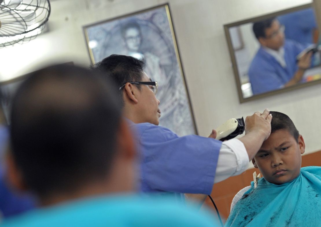 A Thai barber shaving the head of a student near a school in Bangkok on July 31, 2013, shortly after the government relaxed its rules somewhat on student hairstyles.