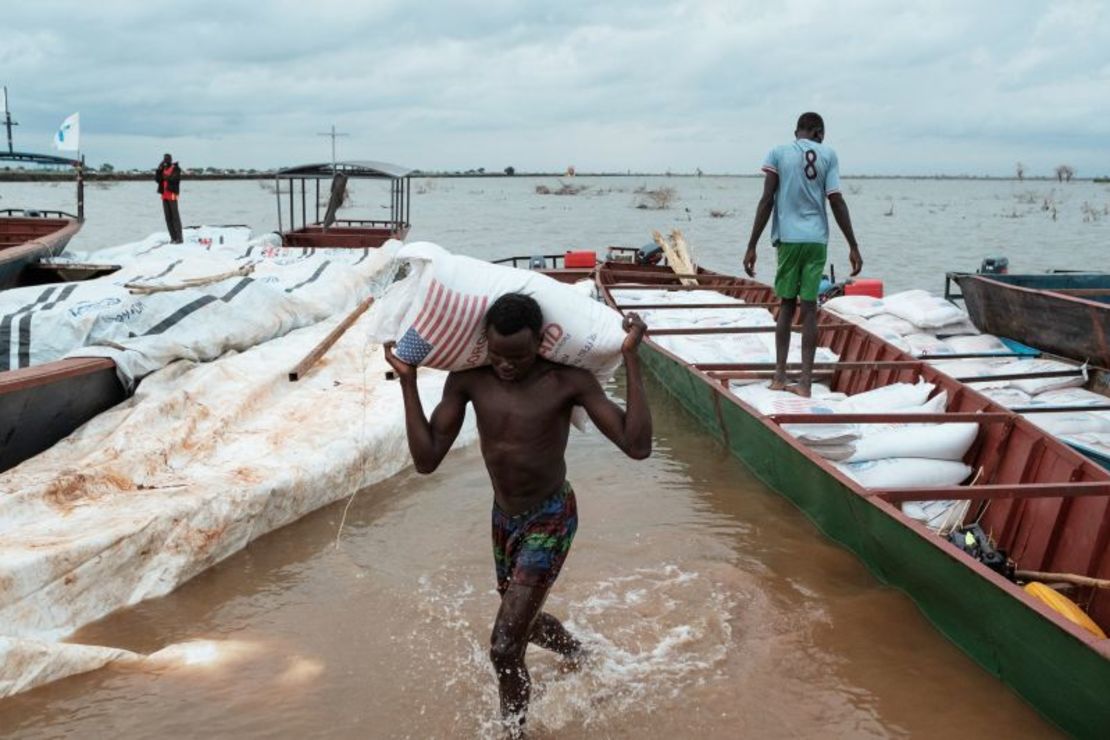 A man carries a 50 kg bag of Sorgo from Usaid delivered to an improvised port to face the waters of the flood near the camp of displaced in Bentiu, South Sudan, in July 2023.