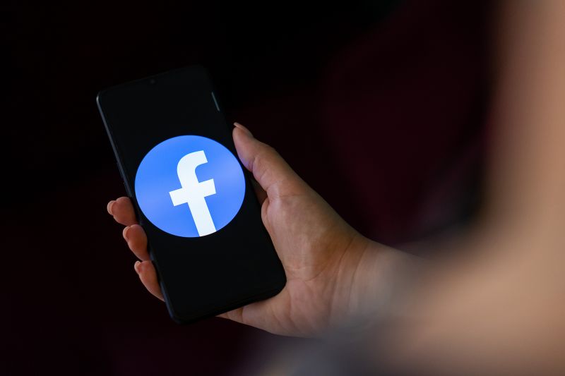 A hand holding a mobile phone with the logo of Facebook on its screen.