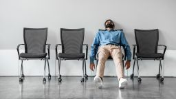 Bored and disappointed male indian employee sitting in waiting room on row of chairs, feeling tired and upset, full length shot, free space