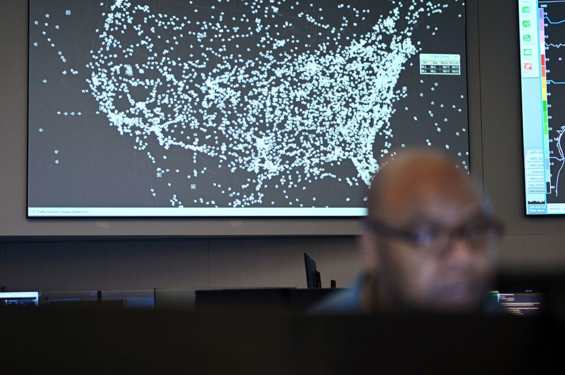 A screen showing current air traffic activity appears behind Stephen Wilson as he works in an FAA air traffic control command center in Washington, DC.