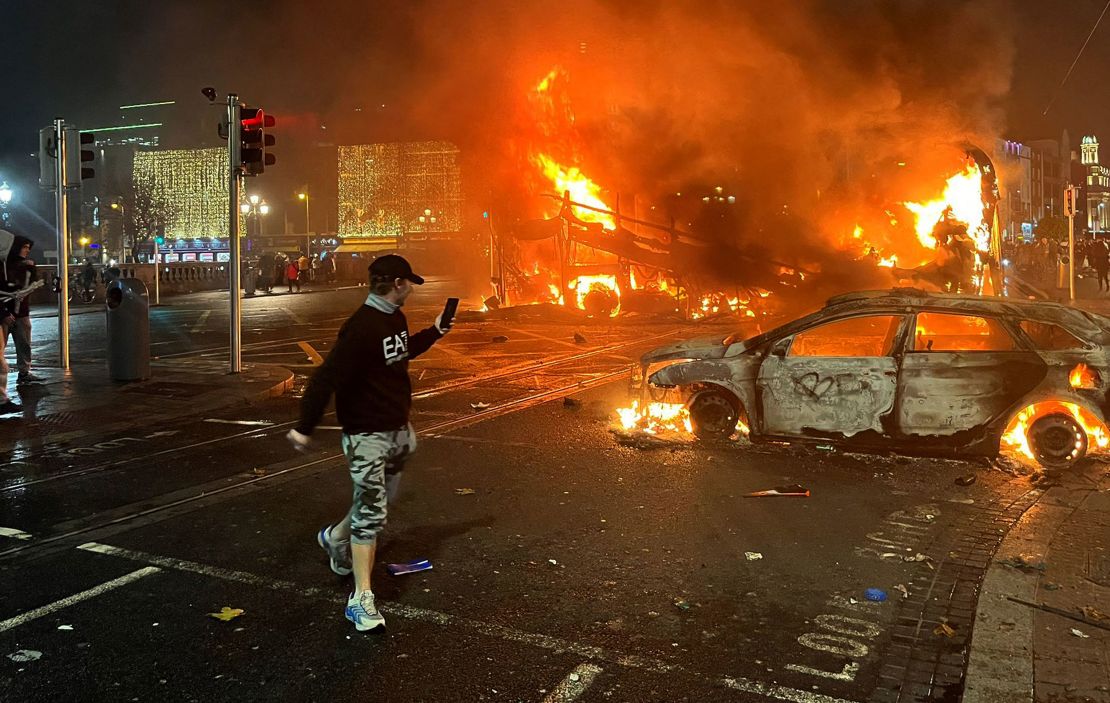 Flames rise from a car and a bus, set alight at the junction of Bachelors Walk and the O'Connell Bridge, in Dublin on November 23, 2023, as people took to the streets in protest following the stabbings earlier in the day.