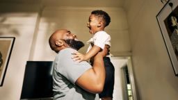Joyous Embrace as a Beaming Father Lifts His Gleeful Son High in a Sunlit Corridor of Their Home