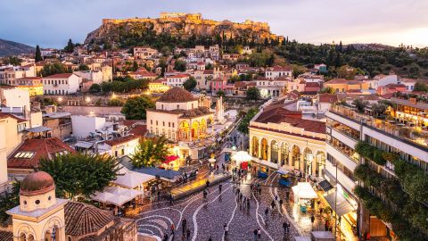 A high angle cityscape of Athens, with Monastiraki Square in the foreground, and the Parthenon on the Acropolis on the horizon.