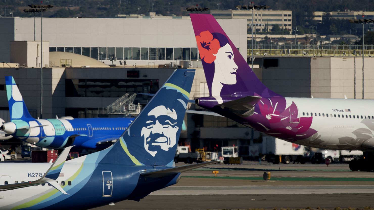 An Alaska Airlines airplane and a Hawaiian Airlines airplane at Los Angeles International Airport (LAX) in Los Angeles, California, US, on Tuesday, Dec. 5, 2023. Alaska Air Group Inc. agreed to buy rival Hawaiian Holdings Inc. for $1.9 billion in cash and debt.