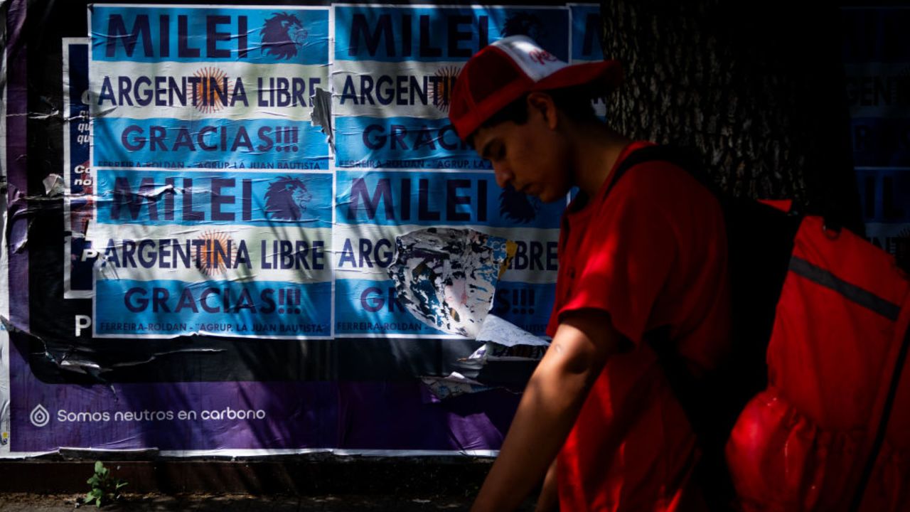 BUENOS AIRES, ARGENTINA - NOVEMBER 30: A food delivery boy stands by signs that read in Spanish "Milei, Free Argentina, Thanks!" on November 30, 2023 in Buenos Aires, Argentina. President-elect Javier Milei of La Libertad Avanza will take office on Sunday 10, replacing incumbent peronist Alberto Fernandez. Milei is a self-described "anarcho-capitalist" libertarian who wants to sharply reduce the size of the State and replace the local peso with the American dollar. During the campaign, he promised to uproot Argentina's political establishment and to align the economy with dramatic measures such as closing the Central Bank. After defeating the current Minister of Economy Sergio Massa in the run-off with 55,65% of the votes, the president-elect has shown moderation and pragmatism as he works on the line up of his cabinet. The new istration will face the challenge to reduce the country's 140% annual inflation and its 44,7% of poverty, as recently announced by a study carried out by ODSA-UCA. (Photo by Tomas Cuesta/Getty Images)