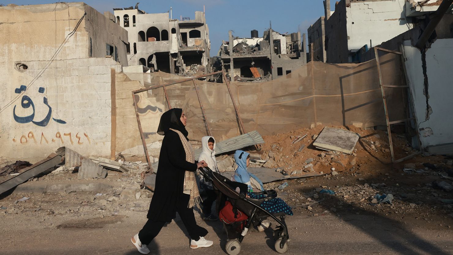 A woman walks her children past buildings destroyed by Israeli bombardment in Rafah in the southern Gaza Strip on December 12, 2023, amid continuing battles between Israel and the militant group Hamas.