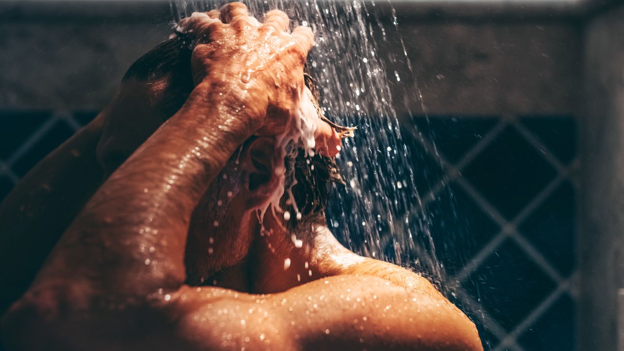 Engrossed in his grooming ritual, a man rinses his hair, the water's embrace enhancing the meditative quality of his daily routine.