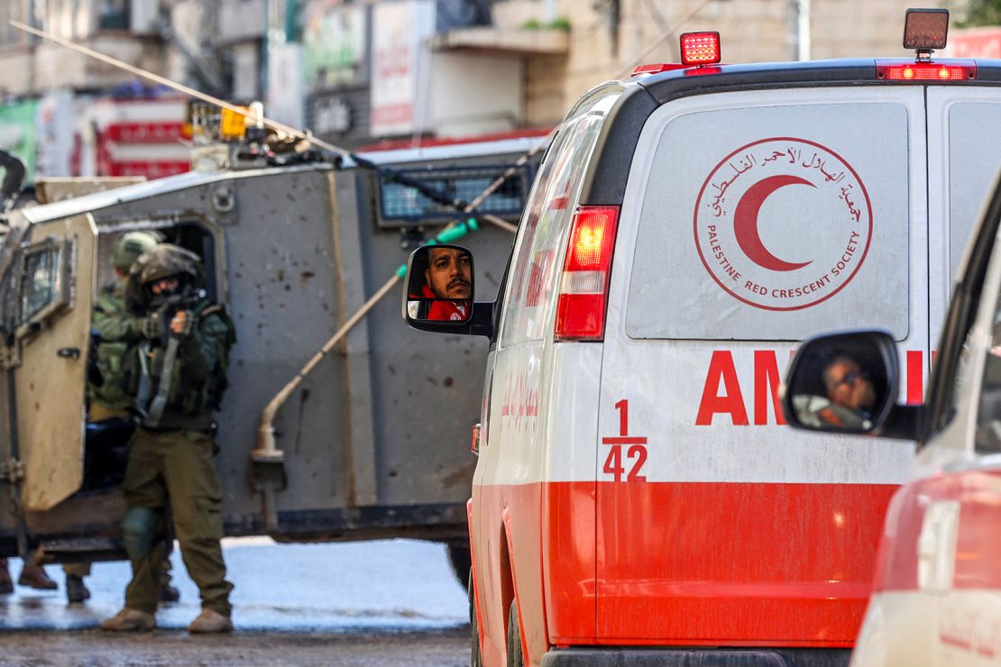 An Israeli soldier aims his weapon as Palestinian Red Crescent ambulances wait on December 13, 2023, in Gaza.