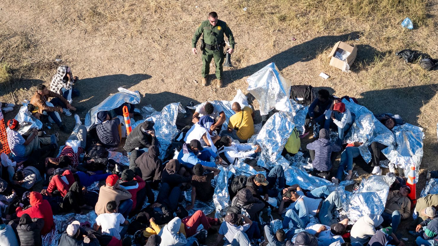 A US Border Patrol agent speaks with immigrants waiting to be processed after crossing from Mexico into the United States on December 17, in Eagle Pass, Texas. 