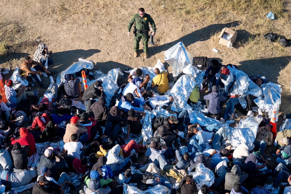 A US Border Patrol agent speaks with immigrants waiting to be processed after crossing from Mexico into the United States on December 17, in Eagle Pass, Texas. 