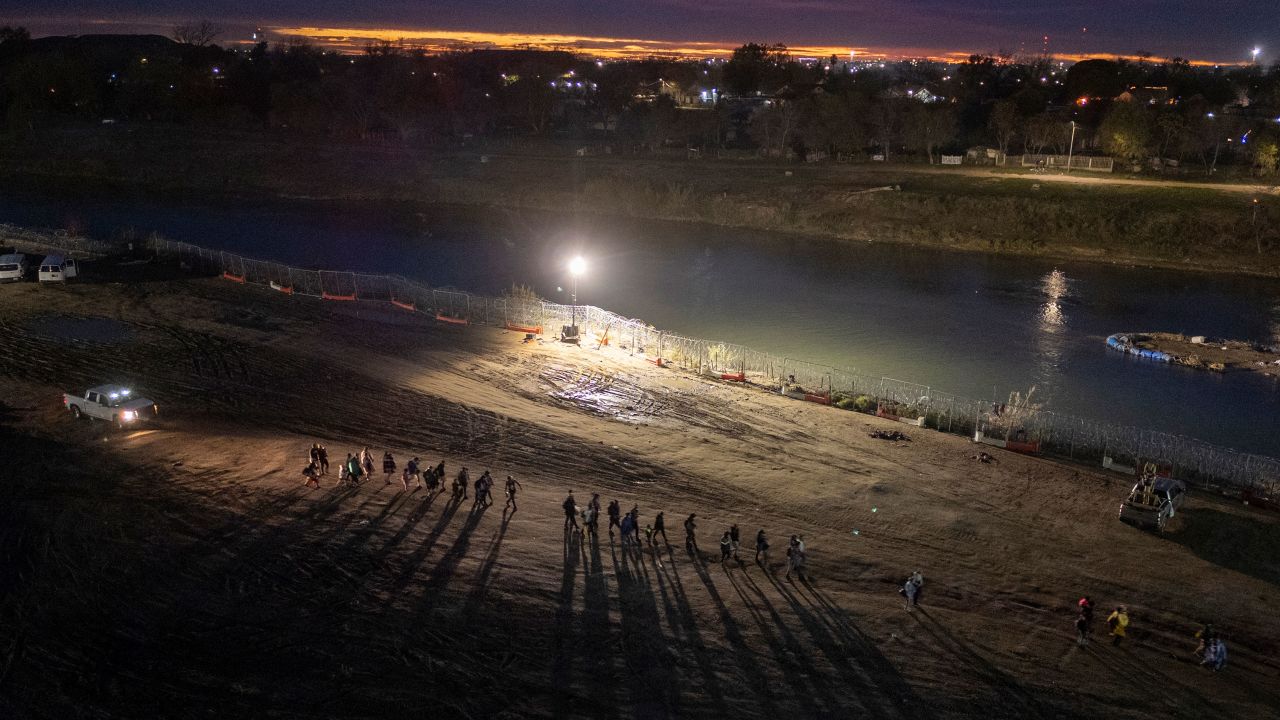 EAGLE PASS, TEXAS - DECEMBER 18: Migrants who had crossed the Rio Grande from Mexico walk towards a processing center on December 18, 2023 in Eagle Pass, Texas. A surge as many as 12,000 immigrants per day crossing the U.S. southern border has overwhelmed U.S. immigration authorities in recent weeks. (Photo by John Moore/Getty Images)