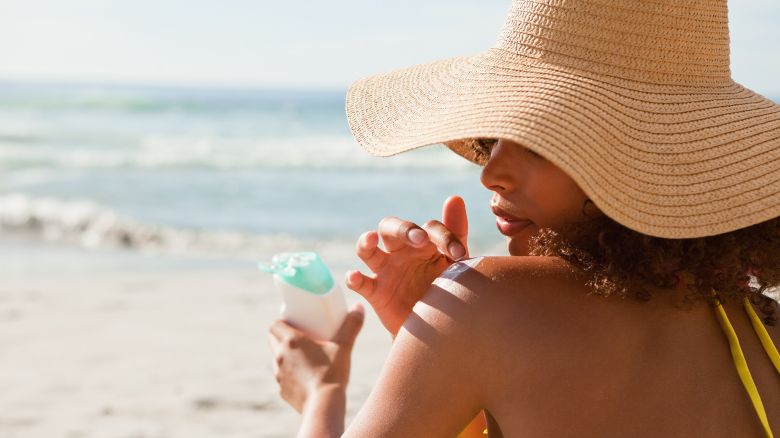 Young beautiful woman applying sunscreen on her shoulder while sitting on the beach